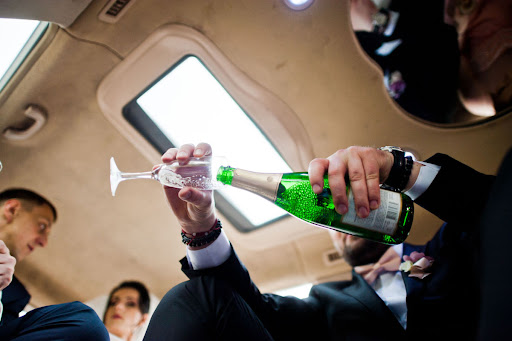 A man in a suit pouring champagne into a bottle inside a vehicle.